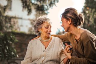 A daughter sits close to her smiling mother in a sunny garden.